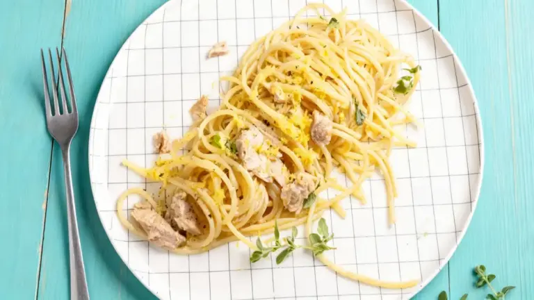 Piatto di spaghetti con tonno, scorza di limone e erbe aromatiche su piatto bianco a griglia