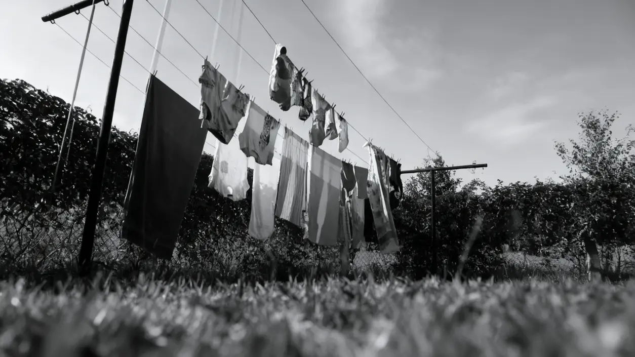 Bucato steso all'aperto su fili tra due pali in un giardino con cielo nuvoloso