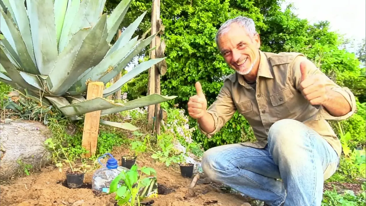 Persona sorridente accanto a un orto con bottiglie usate per irrigazione