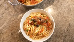 Piatto di spaghetti al tonno con olive e sugo rosso servito in una ciotola bianca